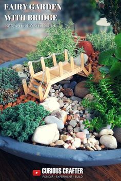 there is a miniature garden in a pot with rocks and plants on it, along with the words fairy garden with bridge