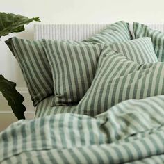 a bed with green and white striped pillows on it's side, next to a plant