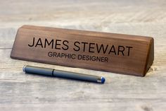 a pen is sitting next to a wooden sign that says, james stewart graphic designer