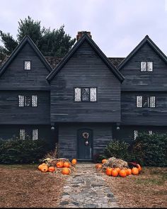 an old black house with pumpkins in the front yard and stone walkway leading up to it