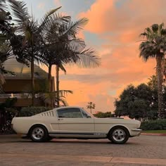 an old car is parked in front of palm trees and the sun sets behind it