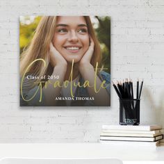 a graduation photo hanging on the wall above a desk with books and pencils in front of it