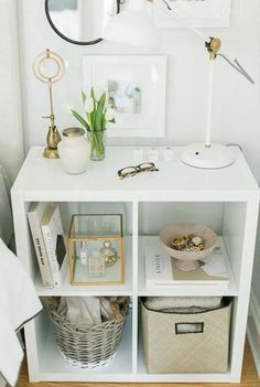 a white shelf with baskets and pictures on it next to a lamp, mirror and other items