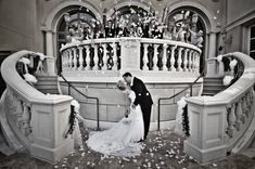 a bride and groom kissing in front of a staircase with rose petals on the ground