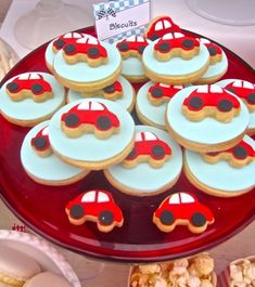 a red plate topped with lots of cookies covered in frosting and decorated like cars