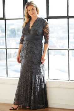 a woman standing in front of a window wearing a long gray dress with sheer sleeves