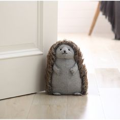 a stuffed hedge sitting on the floor next to an open door with its head sticking out