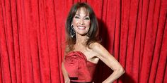 a woman standing in front of a red curtain with her hands on her hips and smiling