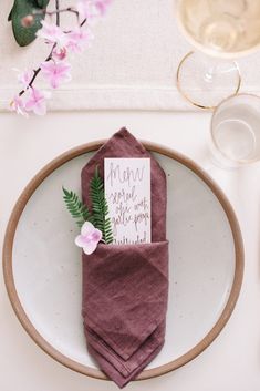 a place setting with napkins, flowers and wine glasses on the table for guests to enjoy