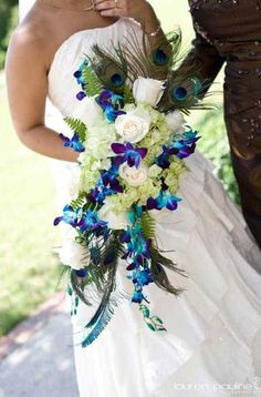 a woman in a wedding dress holding a bouquet with peacocks and flowers on it