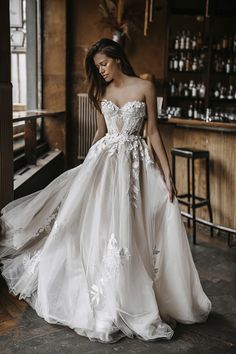 a woman in a white wedding dress standing next to a bar and looking down at the floor