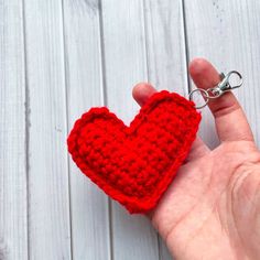 a hand holding a red crocheted heart keychain on a white wooden background