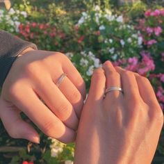 two people holding hands in front of some flowers and plants with their wedding rings on their fingers