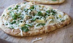 two flat bread pizzas with cheese and spinach on a wooden cutting board next to each other