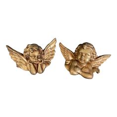 two gold angel statues sitting next to each other on a white background with one holding the other's head