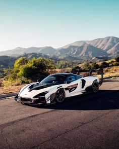 a white and black sports car driving down the road with mountains in the background at sunset