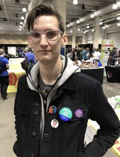 a young man wearing glasses standing in front of a table full of people with badges on them