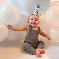 a baby wearing a birthday hat sitting in front of balloons