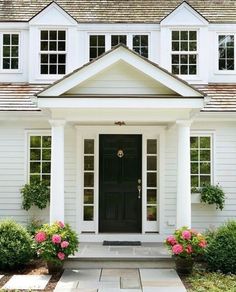 a white house with black front door and flowers on the side walk in front of it