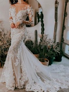 a woman wearing a wedding dress with long sleeves and flowers on the skirt is standing in front of a mirror