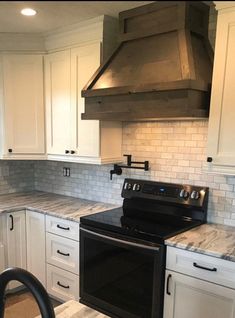 a kitchen with white cabinets and marble counter tops, black stove top oven and range hood