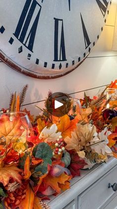 a large clock mounted to the side of a wall next to autumn leaves and candles