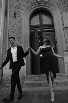 a man and woman are holding hands while walking down the street in front of a building