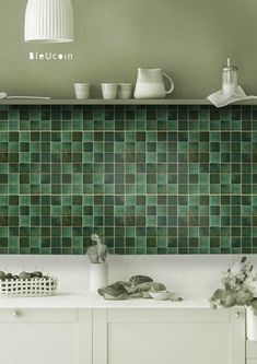 a green tiled wall in a kitchen with white cabinets and counter tops, along with dishes on the shelf