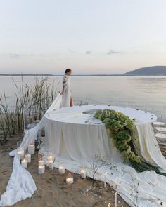 a woman standing on top of a white table covered in flowers and greenery next to candles