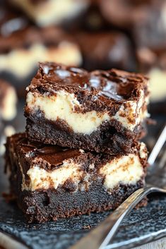 two pieces of chocolate cheesecake brownies on a plate with a fork next to them