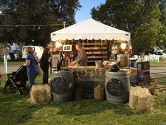 people are standing around in the grass near barrels with wine bottles on them and lights strung up above them