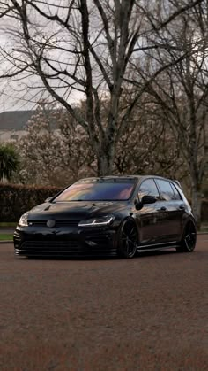 a black car is parked on the side of the road in front of some trees