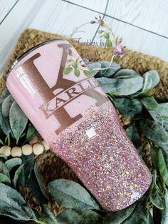 a pink glitter tumbler with the letter y on it sitting next to some leaves