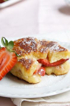 a white plate topped with pastries covered in powdered sugar and sliced strawberries