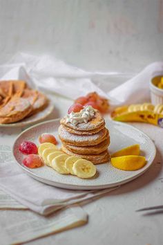 a plate topped with pancakes covered in powdered sugar next to sliced bananas and fruit