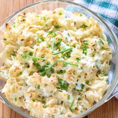 a glass bowl filled with macaroni salad on top of a wooden table next to a blue and white checkered napkin