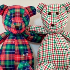 two colorful teddy bears sitting next to each other on a white surface and one is wearing a red, green, and blue checkered shirt