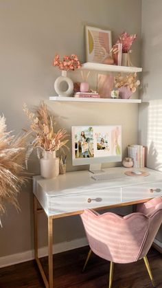 a desk with a computer and some flowers on it in front of a wall mounted shelf