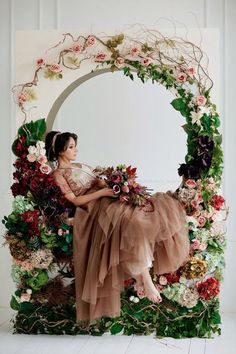 a woman is sitting in front of a flower arch with flowers and greenery around her