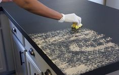 a person in white gloves is cleaning the counter top on a black kitchen island with yellow flowers