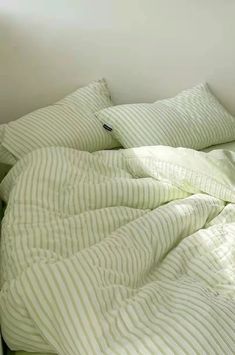 an unmade bed with green and white striped sheets