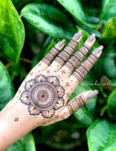 a woman's hand with henna on it and green leaves in the background