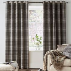 a living room filled with furniture and a window covered in plaid drapes next to a white couch