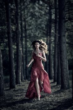 a woman in a red dress is running through the woods with her hair blowing in the wind