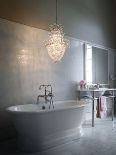 a white bath tub sitting under a chandelier in a bathroom