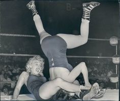 two women are wrestling in an old black and white photo, one has her leg up on the other