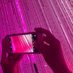 a person taking a photo with their cell phone in front of pink lights and curtains