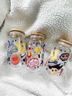 three glass jars with cartoon images on them sitting on a white blanket next to each other