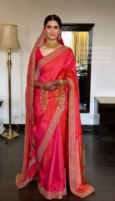 a woman in a pink and red sari with gold jewelry on her neck, standing next to a lamp