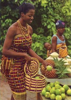 a woman standing in front of a table filled with pineapples and other fruit